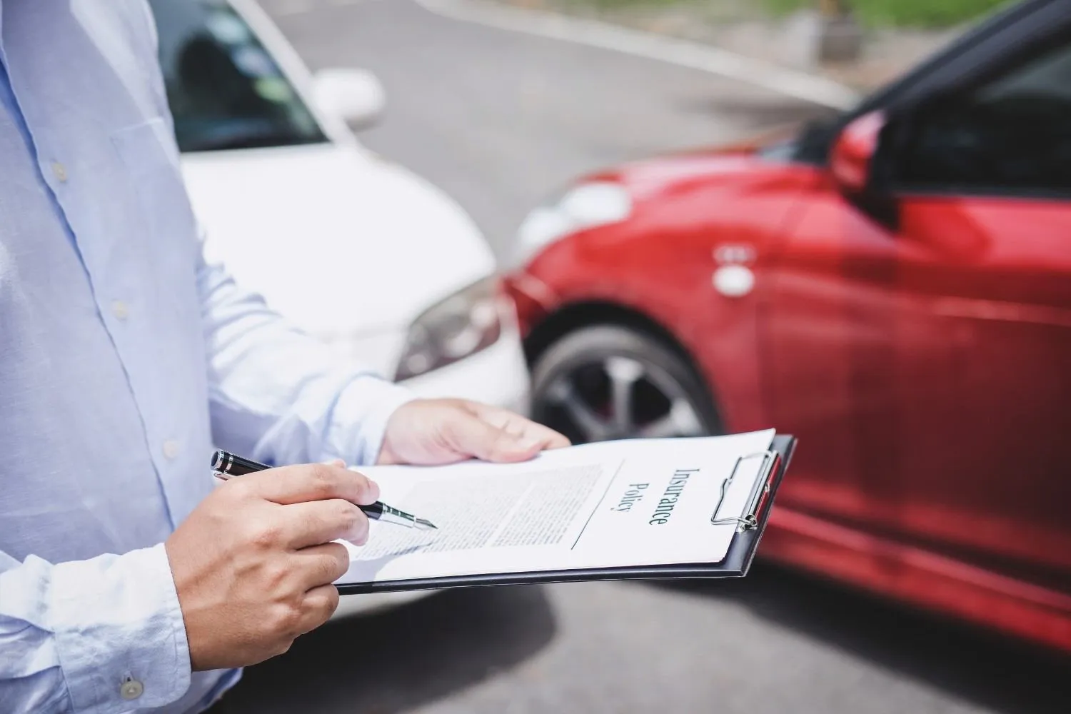 Insurance policy being filled in on a clipboard beside two cars