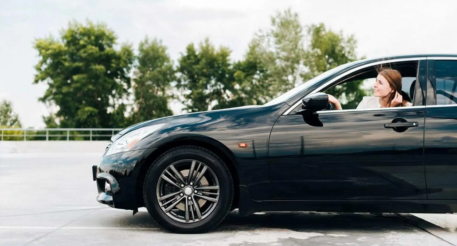 Driver at the wheel of a black sedan on an open lot